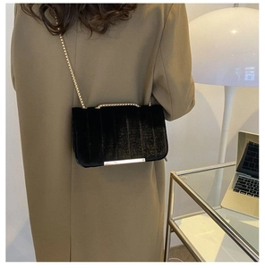 Detail of a black velvet crossbody bag featuring golden chain and quilted stripe texture