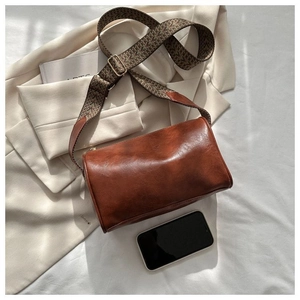 Detailansicht der braunen Zylindertasche mit gewebtem Gurt neben einem Smartphone