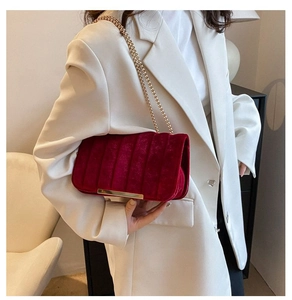 Detail of red velvet crossbody bag featuring golden chain and metallic trim on the flap