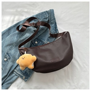 Detail of a dark brown half-moon crossbody bag with fashion label and plush charm