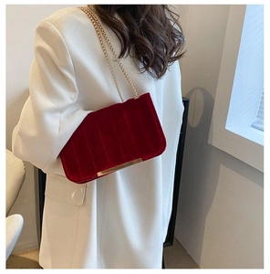 Detail of red velvet shoulder bag with gold chain and vertical striped stitching on model