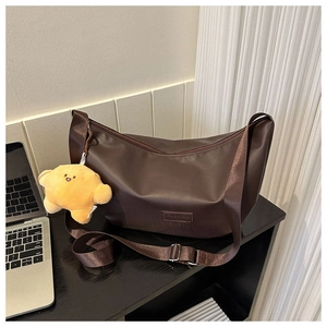 Detail of dark brown dumpling bag with wide strap and yellow croissant plush charm