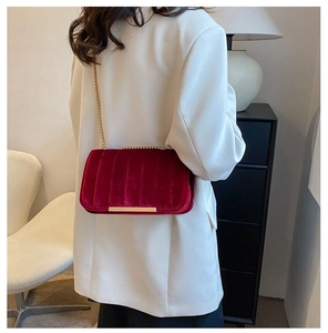 Detailed view of red velvet crossbody bag with gold chain strap on a model shoulder