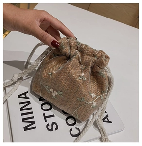 Détail d'un mini sac seau en paille avec broderies florales blanches et cordon de serrage