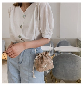 Détail du sac seau en paille avec broderie florale et fermeture à cordon en coton