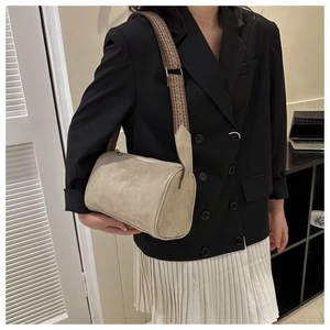 Detail einer beigen Zylindertasche mit breitem gewebtem Gurt an einem weiblichen Model