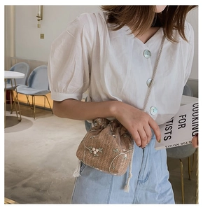 Détail du sac seau en paille avec broderie florale et fermeture par cordon de serrage