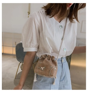 Détail d'un sac seau en paille avec broderies florales blanches et cordons en coton