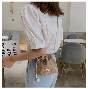 Détail du sac seau en paille avec broderie florale et bandoulière tressée blanche
