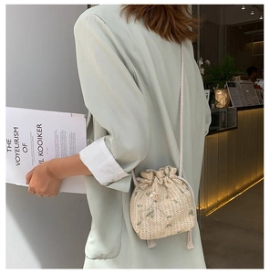 Détail d'un sac seau en paille avec broderie florale et fermeture par cordon de serrage