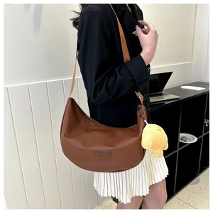 Close-up of brown crescent crossbody bag with PU leather texture and plush croissant charm