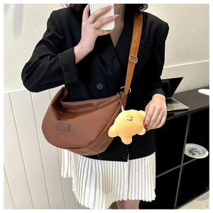 Brown dumpling crossbody bag with wide strap and yellow charm on model in office setting