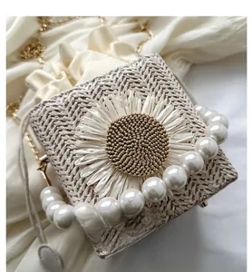 Detail of woven straw bag featuring large daisy floral applique and pearl top handle