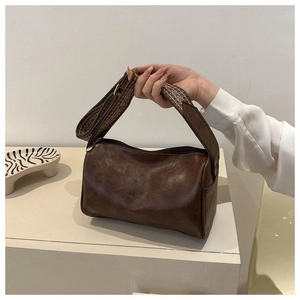 Nahaufnahme der braunen Zylindertasche aus Leder mit breitem Jacquard-Schultergurt