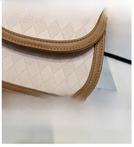 Macro detail of beige perforated leather texture and brown trim stitching on the handbag