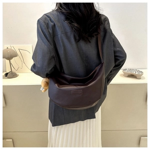 Detail view of a dark brown crescent crossbody bag with embossed fashion label on soft leather