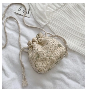 Détail du sac seau en paille avec broderie florale pastel et fermeture par cordon de serrage