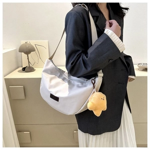 Detail of cream-colored crescent bag with a cute croissant plush charm and adjustable strap