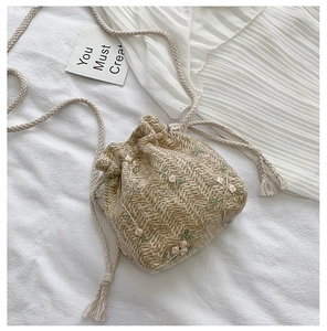 Gros plan du sac seau en paille avec broderie florale rose et cordon à franges