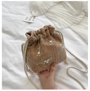 Détail d'un sac seau en paille avec broderies florales roses et cordon en coton blanc