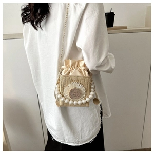 Detail of hand-woven straw crossbody bag with pearl handle and sunflower applique