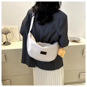 Minimalist white nylon crescent bag with wide strap worn by a model in casual setting