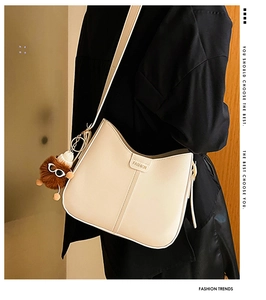Detail of beige bucket bag with wide strap and brown puppy charm on a stylish model