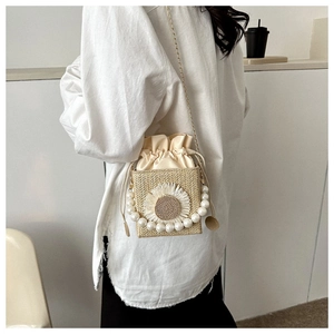 Detail of woven straw crossbody bag with sunflower decor, pearl handle, and gold chain