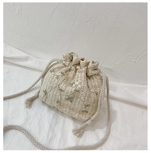 Détail du sac seau en paille avec broderie florale et bandoulière à cordon crème