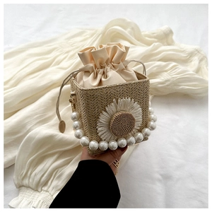 Detail of woven straw bag featuring floral daisy appliqué and elegant pearl top handle