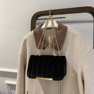Elegant black velvet crossbody bag with gold chain and vertical quilting on beige coat