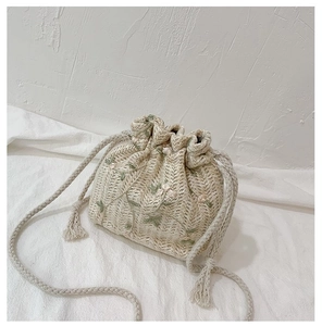 Détail d'un sac seau en paille avec broderies florales et cordon à glands doux