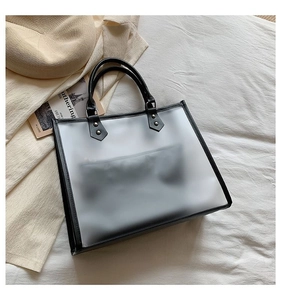 Detail view of transparent tote bag with black trim and inner pouch on minimalist bedding
