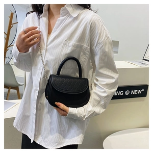 Detail of a black quilted saddle bag with silver chain strap and top handle style