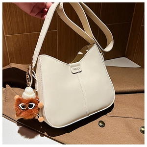 Detail of cream bucket bag with faux leather texture and brown fur ball charm accessory