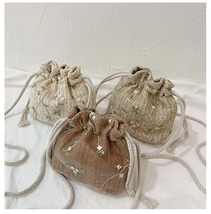 Détail de sacs seaux en paille avec broderie florale blanche et fermeture à cordon