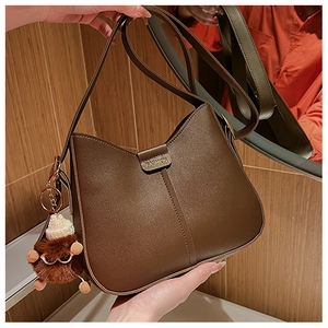 Detailed close-up of a dark brown matte bucket bag with wide strap and plush pendant