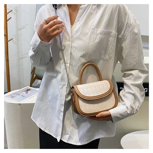 Close-up of quilted beige crossbody bag with metal chain strap and brown handle detail