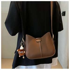 Detail view of a brown bucket bag with wide strap and cute plush doll pendant accessory