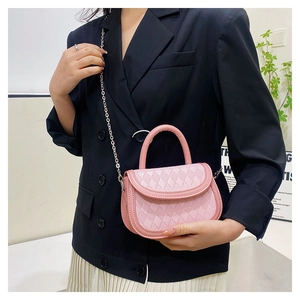 Close-up of pink quilted saddle bag with metal chain strap on model in modern setting
