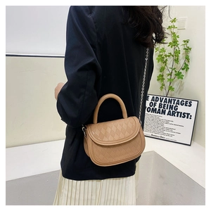 Close-up of a light brown quilted saddle bag with handle and metal chain strap details