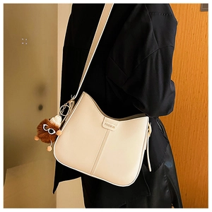 Detail of cream crescent shoulder bag with wide strap and brown plush monster charm