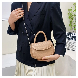 Close-up of beige quilted saddle bag with golden chain and handle on a model