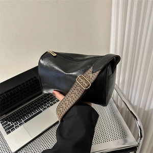 Glänzende schwarze zylindrische Umhängetasche mit breitem Gurt und goldener Hardware