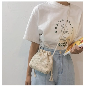 Détail du sac seau en paille tissée beige avec motifs floraux verts et bandoulière en corde