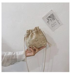 Détail du sac seau en paille avec fleurs blanches tissées et fermeture à cordon réglable