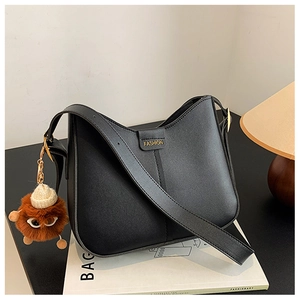 Detail view of black pebbled leather bucket bag with wide strap and brown plush charm