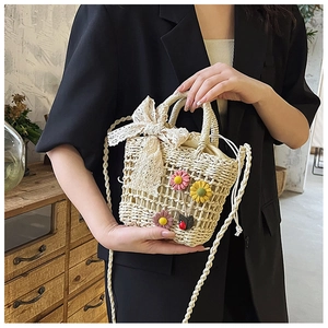 Detail of beige hollow-out straw bucket bag with floral patches and lace bow detail