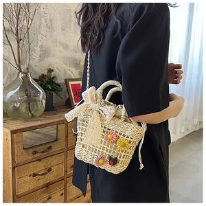 Detail of straw bucket bag with floral accents and a large white lace bow on strap