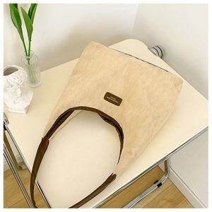 Vue détaillée du canevas matelassé beige et de la bandoulière en cuir brun du sac cabas